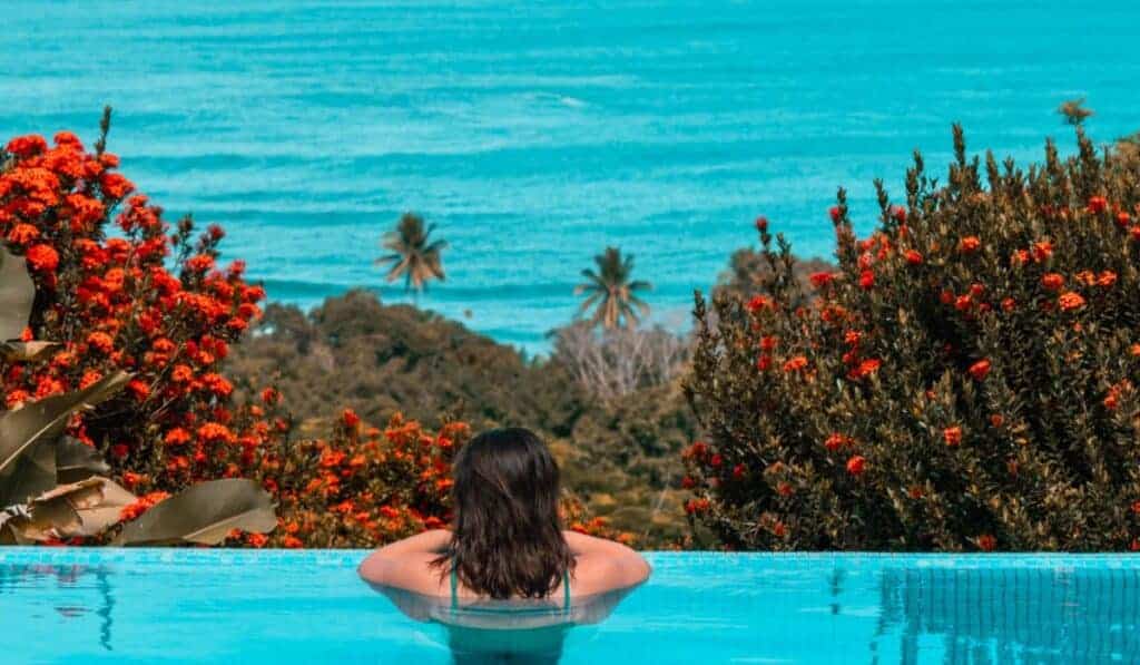 View of woman from behind with brown hair in infinity pool looking at the ocean in Costa Rica